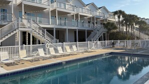 A multi-story hotel with balconies, a swimming pool, and palm trees.