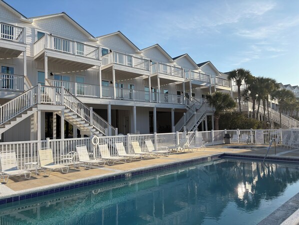 A multi-story hotel with balconies, a swimming pool, and palm trees.