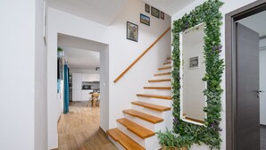 A staircase with wooden steps leading to a landing, flanked by white walls and a mirror with a green leafy border.