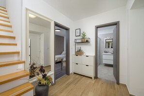 A modern interior with a wooden staircase, a hallway leading to a bedroom, and a bathroom with a mirror and sink.