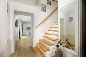 Ein modernes Interieur mit einer Holztreppe, weißen Wänden und einem sichtbaren Küchenbereich im Hintergrund.