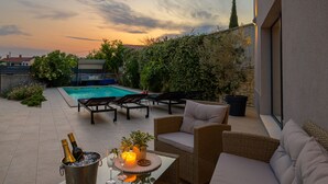A patio with a pool, outdoor furniture, and a table with drinks and candles.