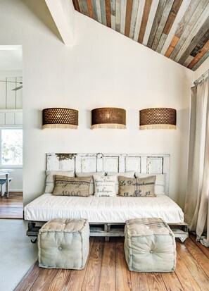 Une chambre avec un lit blanc, trois lampes fixées au mur et des poutres en bois rustique au plafond.