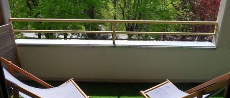 Ein Balkon mit zwei Holzliegen und Blick auf grüne Bäume.