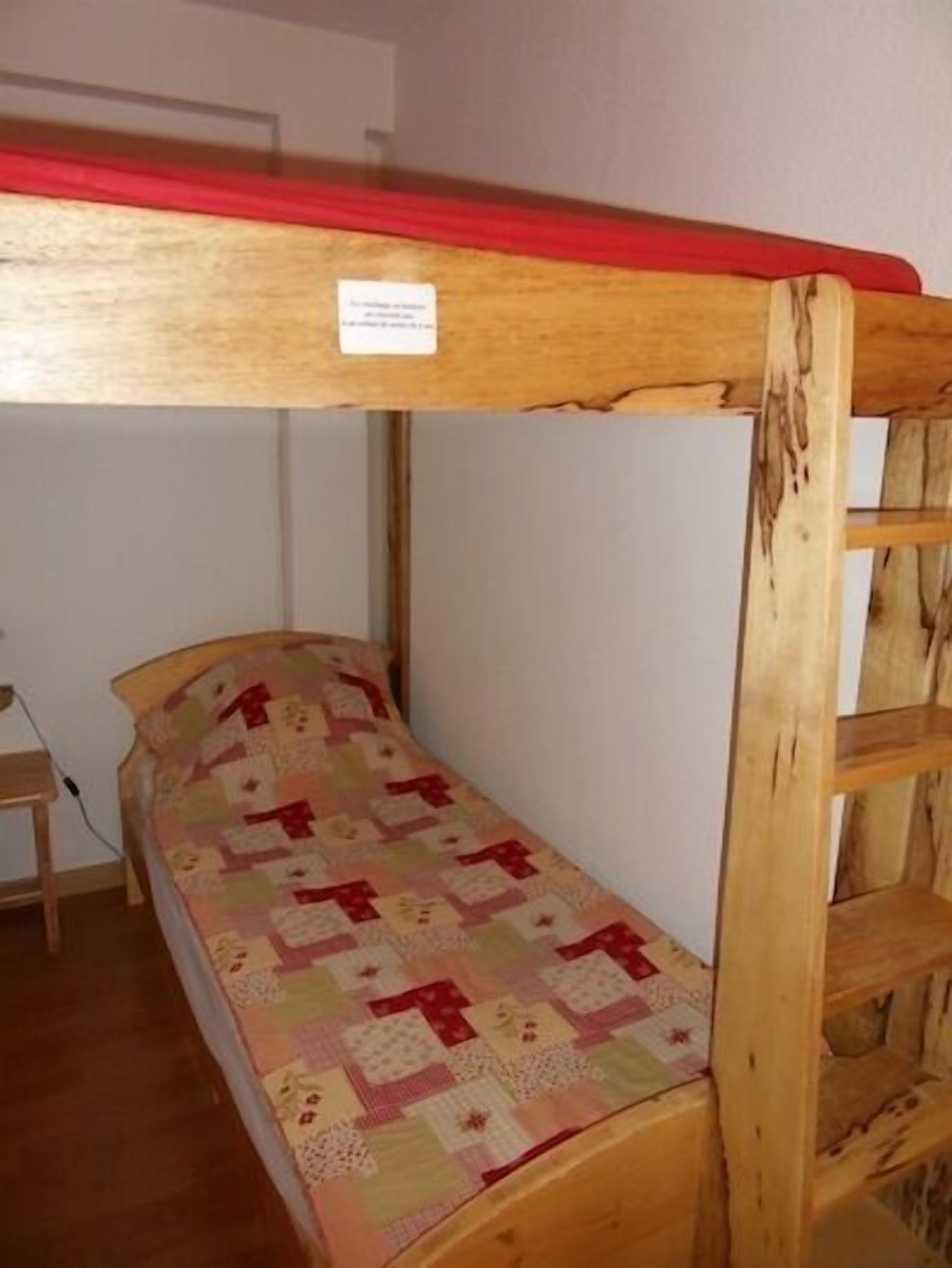 Una cama litera con baranda superior roja, un colchón acolchado y una escalera de madera.