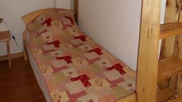 Una cama litera con baranda superior roja, un colchón acolchado y una escalera de madera.