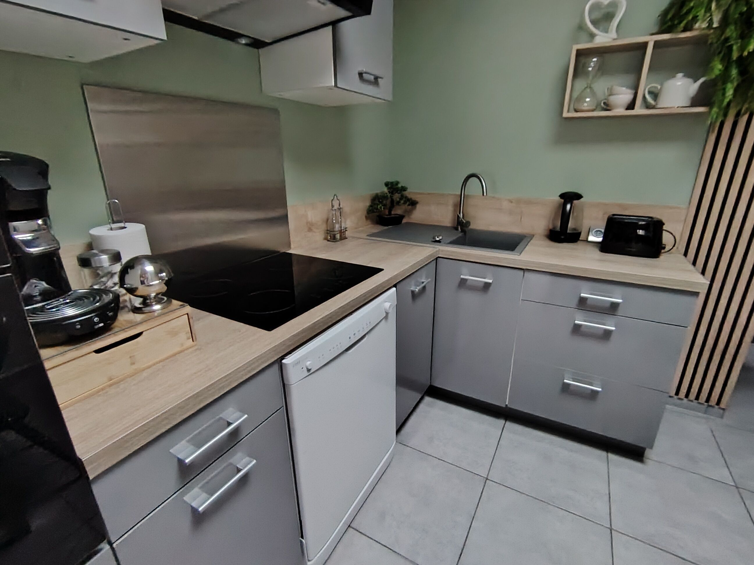 A modern kitchen with a black stove, white dishwasher, and grey cabinets.