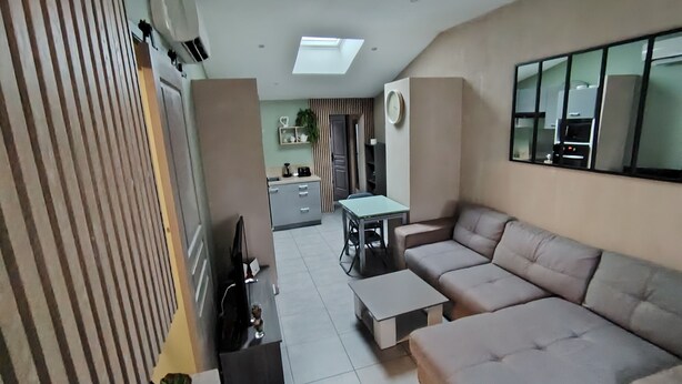 A modern living room with a sofa, a coffee table, and a TV. There is a kitchen in the background with a dining table and chairs. - 50m2 of silence in the heart of Vitrolles (Vitrolles)