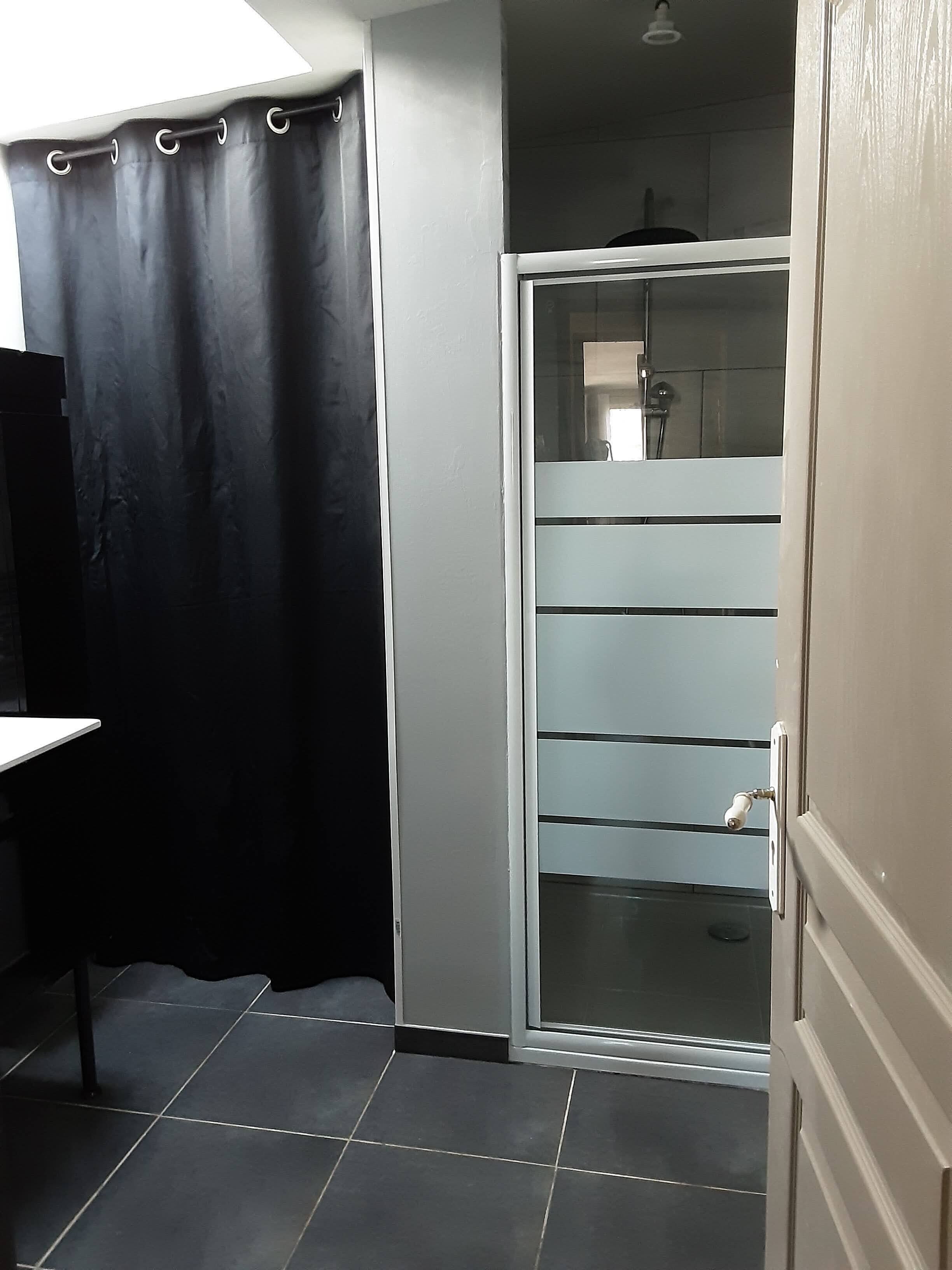 Ein Badezimmer mit Glastür, schwarzem Vorhang und Fliesenboden.