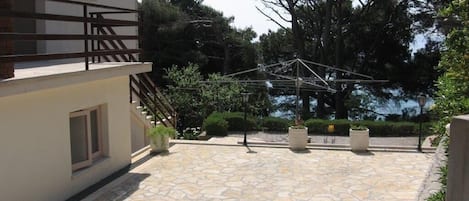 Un patio empedrado con cerca de madera, una pérgola y un gran árbol.