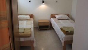 Una habitación pequeña y sencilla con dos camas individuales, una mesita de noche y una lámpara fijada a la pared.