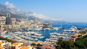 Un port de plaisance où sont amarrés de nombreux bateaux, entouré d’un paysage urbain avec des bâtiments et des montagnes en arrière-plan.
