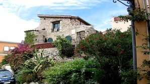 Un bâtiment en pierre doté d’une petite fenêtre et d’une porte, entouré d’une végétation luxuriante et de plantes en fleurs.