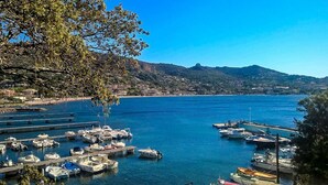 Un port de plaisance où sont amarrés des bateaux, entouré de collines et surplombé d’un ciel bleu clair.