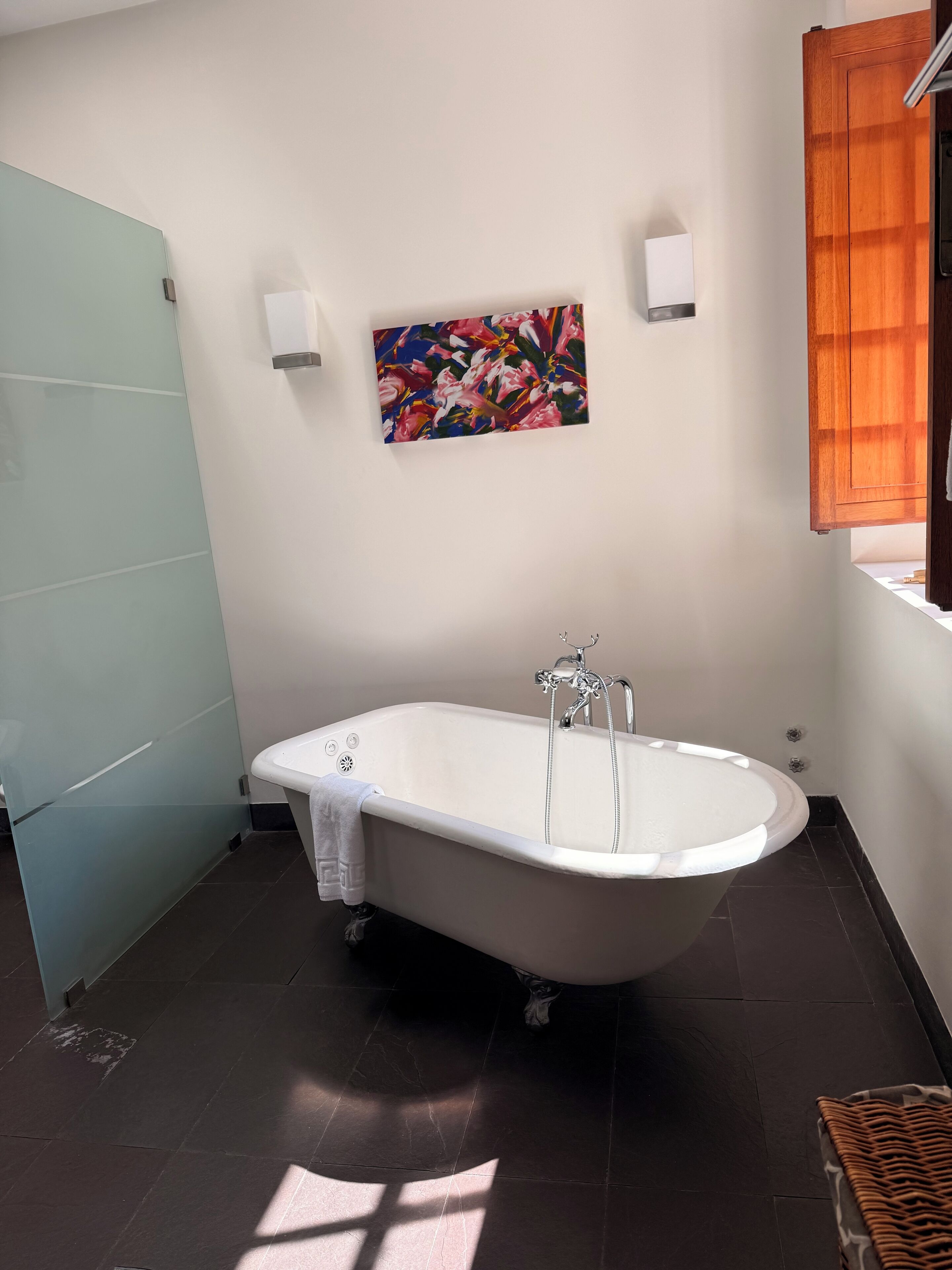 A bathroom with a freestanding bathtub, a glass shower enclosure, and a colorful abstract painting on the wall.