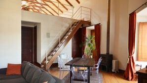 A spacious living area with a wooden staircase, a dining table with chairs, a sofa, and a potted plant.