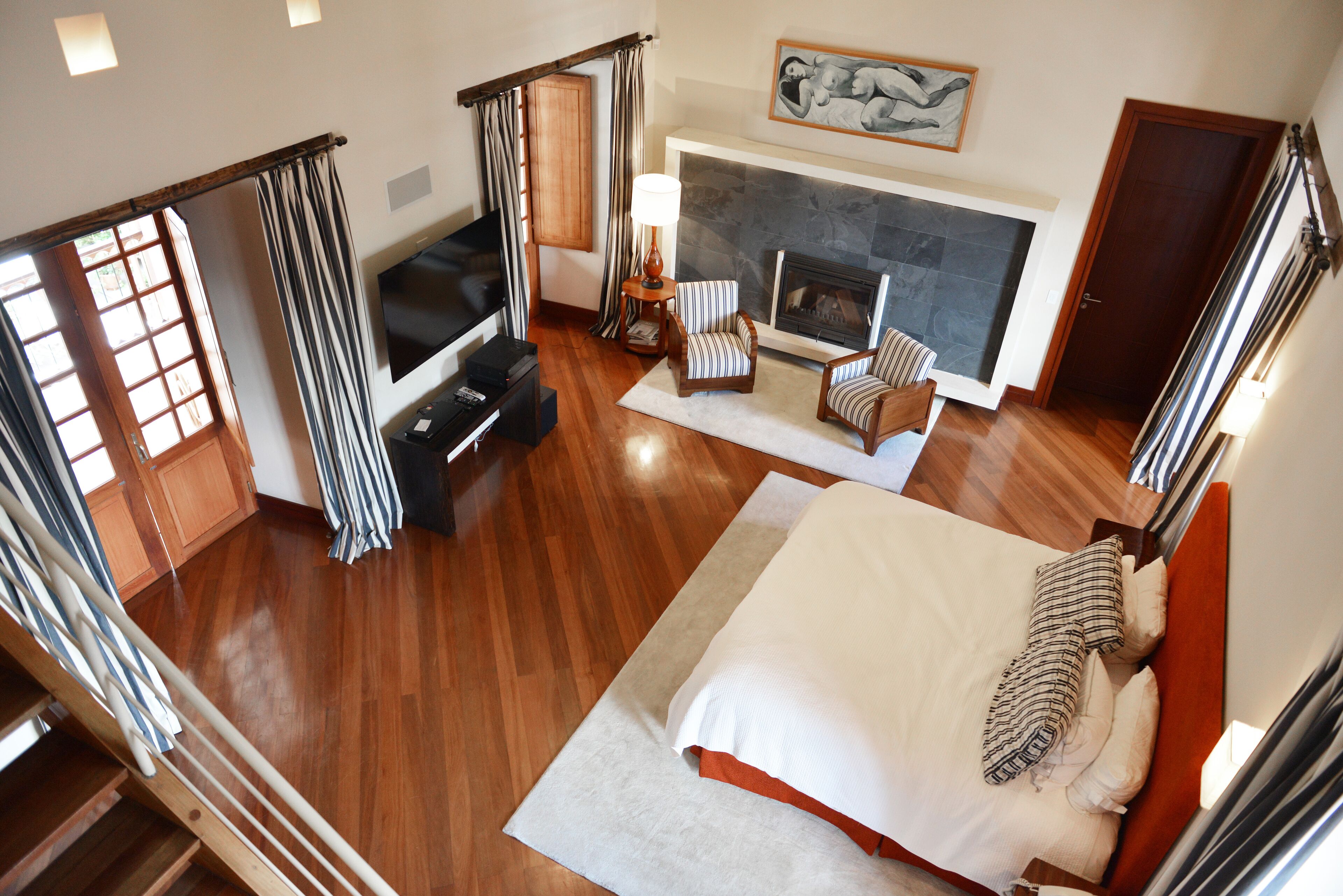 Ein geräumiges Schlafzimmer mit einem großen Bett, einem Kamin, einem Fernseher und einer Treppe.