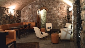A stone-walled lounge with a high arched ceiling, cushioned seating, and a candelabra.