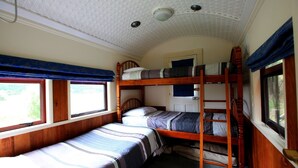 A bunk bed room with two beds, a window, and a ceiling light fixture. - Waitomo Express - 1918 Train Carriage (Waitomo)