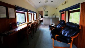 A train carriage with wooden seating, a small kitchenette, and a dining area. - Waitomo Express - 1918 Train Carriage (Waitomo)