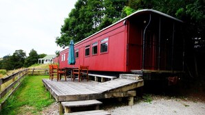 A red building with a wooden deck and outdoor seating area. - Waitomo Express - 1918 Train Carriage (Waitomo)