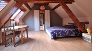 Ein Schlafzimmer mit schrägem Dach, Holzbalken, einem Bett mit Punkte-Bettwäsche, einem Schreibtisch mit Stuhl und einem Fenster.