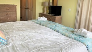 A neatly made bed with a quilt, a television on a stand, a mirror, and a door in the background. - 167 Beach Club Villa - Marsh & Canal View - Golf Cart Included (Fripp Island)