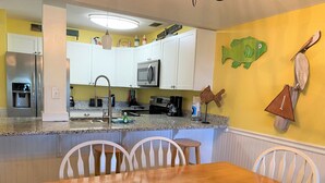 A kitchen with white cabinets, a microwave, and a coffee maker. There is a dining table with chairs and a fish decoration on the wall. - 167 Beach Club Villa - Marsh & Canal View - Golf Cart Included (Fripp Island)