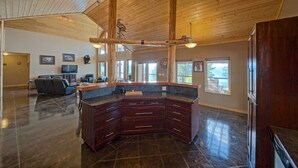 A spacious kitchen with dark wooden cabinets, a large island, and a high ceiling with exposed beams. - Stunning Post and Beam Home with the best views in the valley, wheelchair acc. (Penticton)