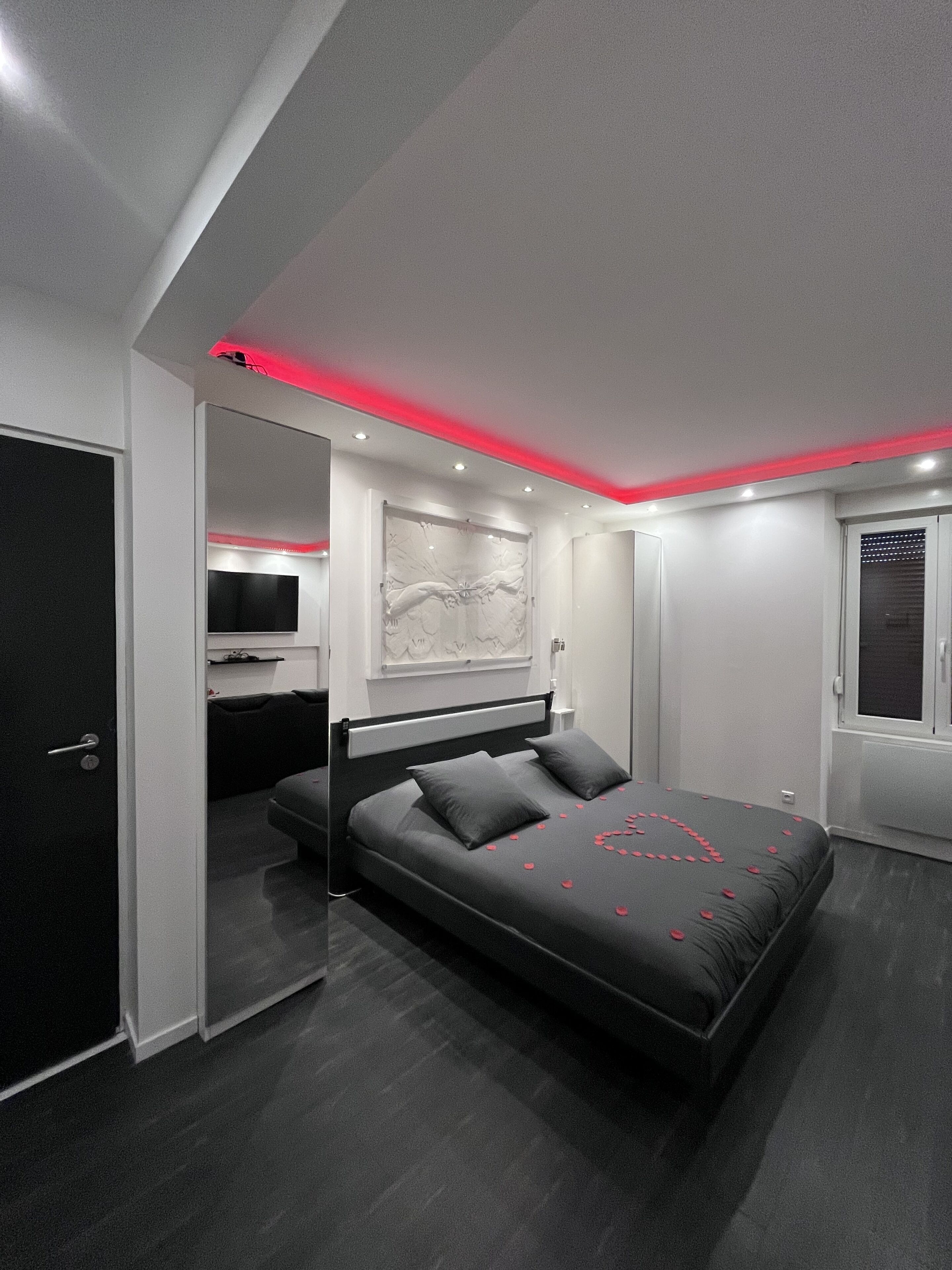Une chambre moderne avec un grand lit, un téléviseur à écran plat et un plafond doté d’un éclairage rouge.