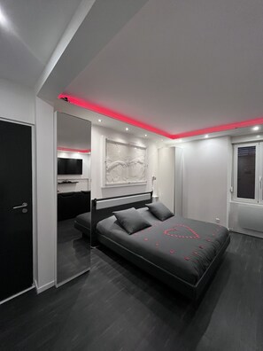 A modern bedroom with a large bed, a flat-screen TV, and a ceiling with red lighting. - Fully privatized apartment with jacuzzi and steam shower (Colmar)
