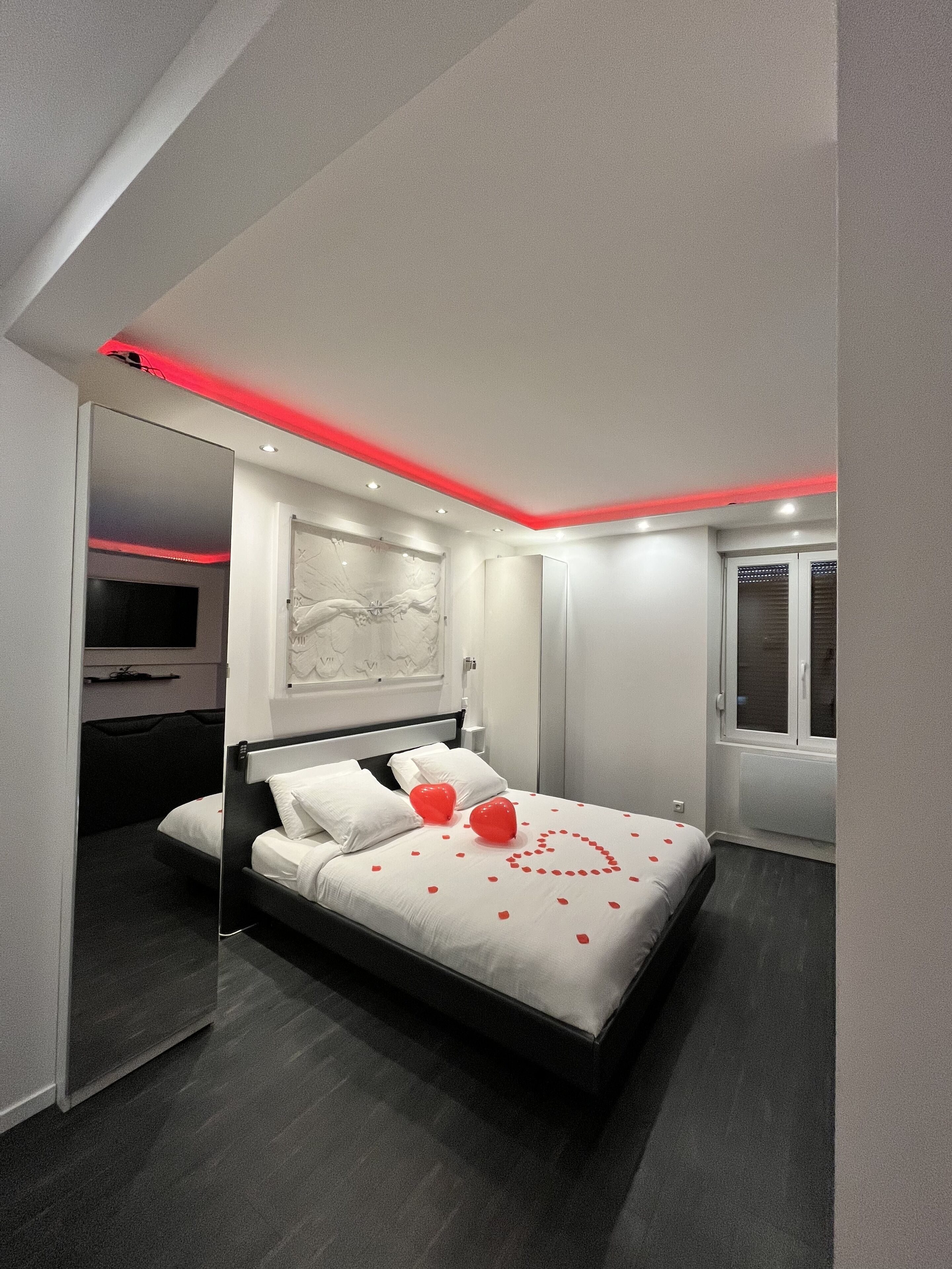 A modern bedroom with a bed, a nightstand, a wall-mounted TV, and a window with blinds.