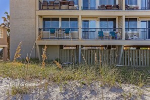A multi-story building with balconies, outdoor seating, and a sandy ground.