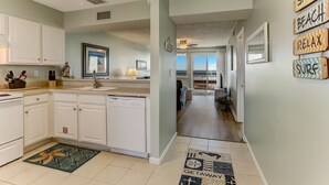 A kitchen with white cabinets, a dishwasher, and a countertop with kitchen utensils. There is a window with a picture frame and a ceiling fan.