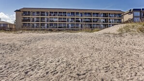 A multi-story hotel with balconies, located near a sandy beach.
