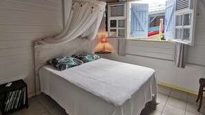 Un dormitorio con cama a dosel, una mesita con lámpara y una ventana con contraventanas.