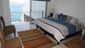 A bedroom with a bed, a chair, a nightstand with a lamp, and a view of the sea through a balcony. - Beautiful home with private beach just for rest and relaxation. (Manzanillo)