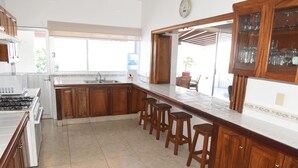 A kitchen with wooden cabinets, a large island with stools, a built-in oven, and a window providing natural light. - Beautiful home with private beach just for rest and relaxation. (Manzanillo)