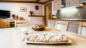 A kitchen with wooden cabinets, a dining table with a loaf of bread, a bowl of fruit, and a small white bowl. - Ski and hiking adventure in the immediate vicinity, away from the crowds, yet close to the center (Selva Gardena - Wolkenstein in Gröden)