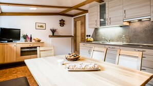 A modern kitchen with wooden cabinets, a dining table, and a television on the left. - Ski and hiking adventure in the immediate vicinity, away from the crowds, yet close to the center (Selva Gardena - Wolkenstein in Gröden)