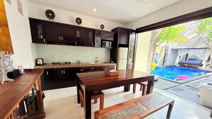 Una cocina moderna con armarios oscuros, una mesa de comedor de madera y vistas a una piscina.