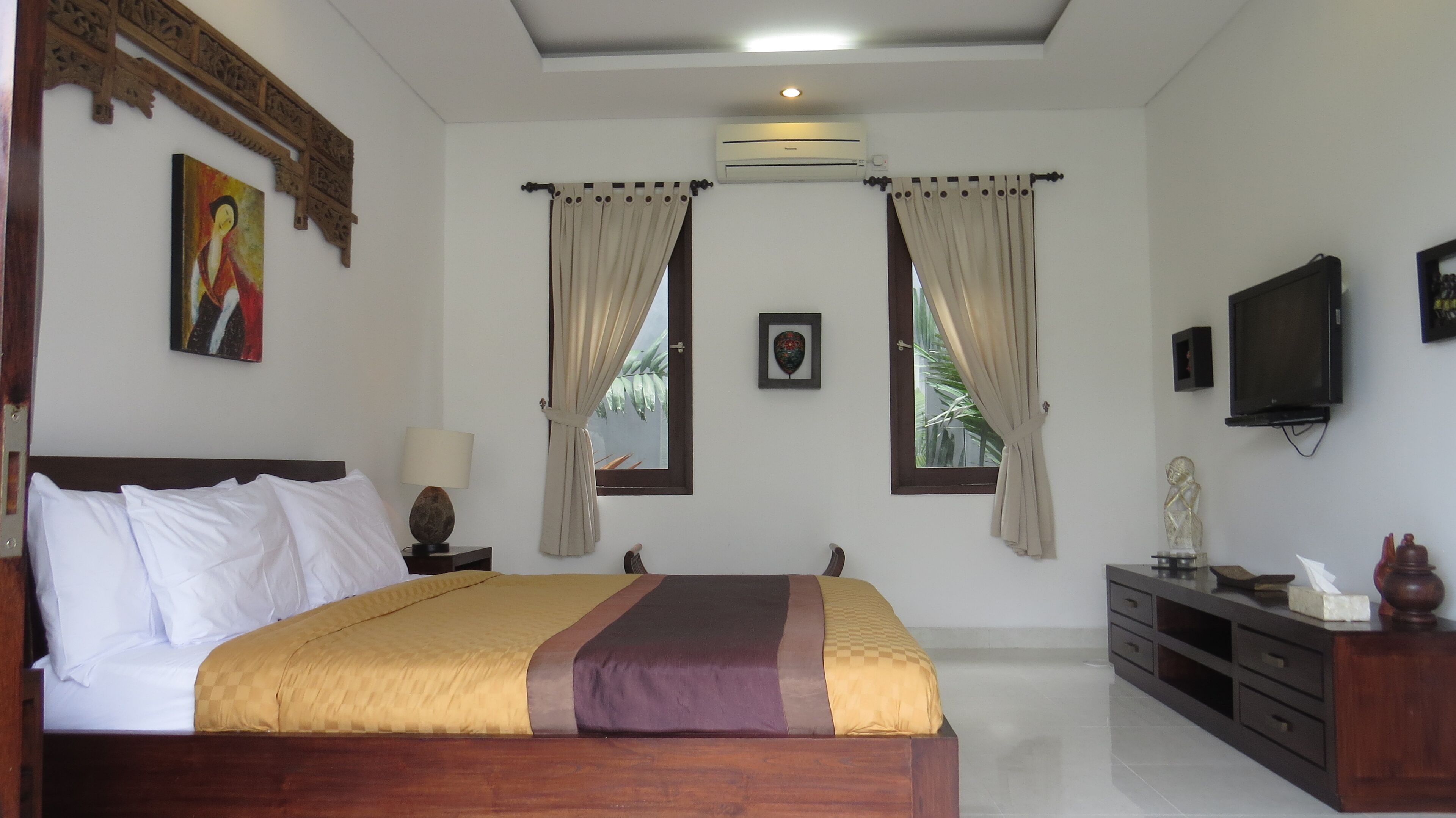 A bedroom with a large bed, a nightstand, a TV, and an air conditioning unit.