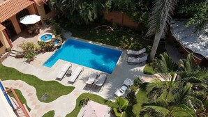 Piscina com espreguiçadeiras e uma pequena fonte, cercada por palmeiras e um espaço de estar ao ar livre.