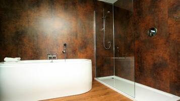 Un baño moderno con una bañera independiente, ducha con mampara de cristal y suelo de madera.