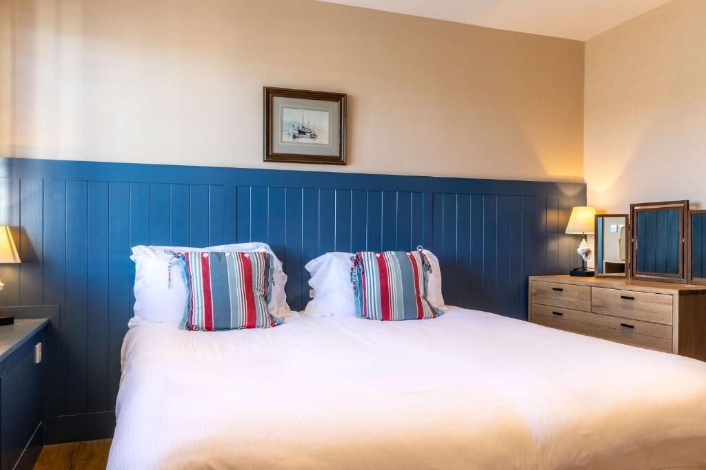 Ein Hotelzimmer mit Bett, Nachttisch, Kommode und einem gerahmten Bild an der Wand.