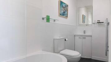 Ein modernes Badezimmer mit Badewanne, Toilette und einer Glasablage für Pflegeprodukte.