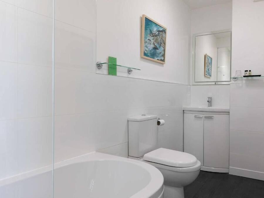 Ein modernes Badezimmer mit Badewanne, Toilette und einer Glasablage für Pflegeprodukte.