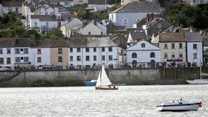 A coastal town with buildings along the waterfront, a sailboat, and a small motorboat. - Seagate (Bideford)