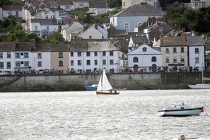 Un pueblo costero con edificios a lo largo del malecón, un velero y un pequeño barco a motor.