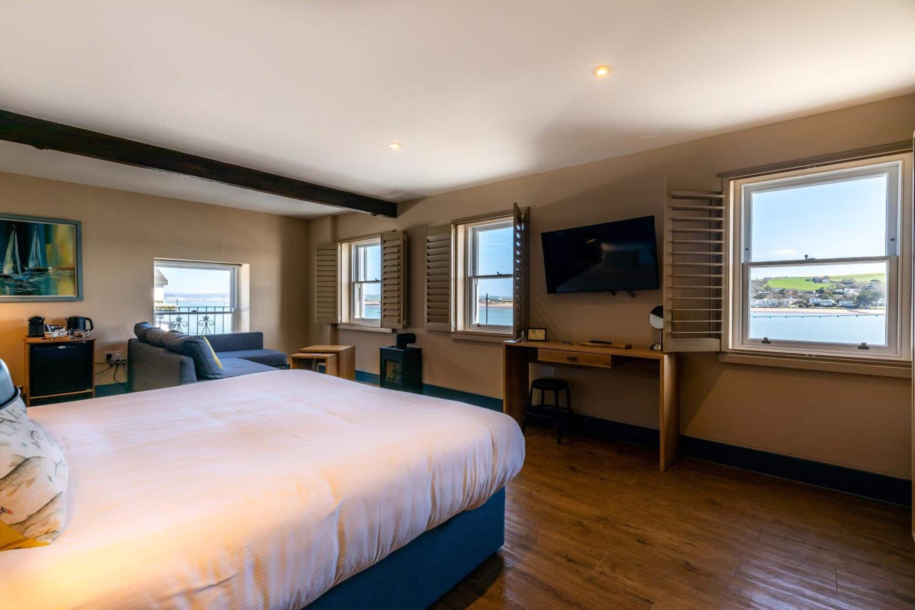A bedroom with a large bed, a desk, a TV, and a view of the sea.